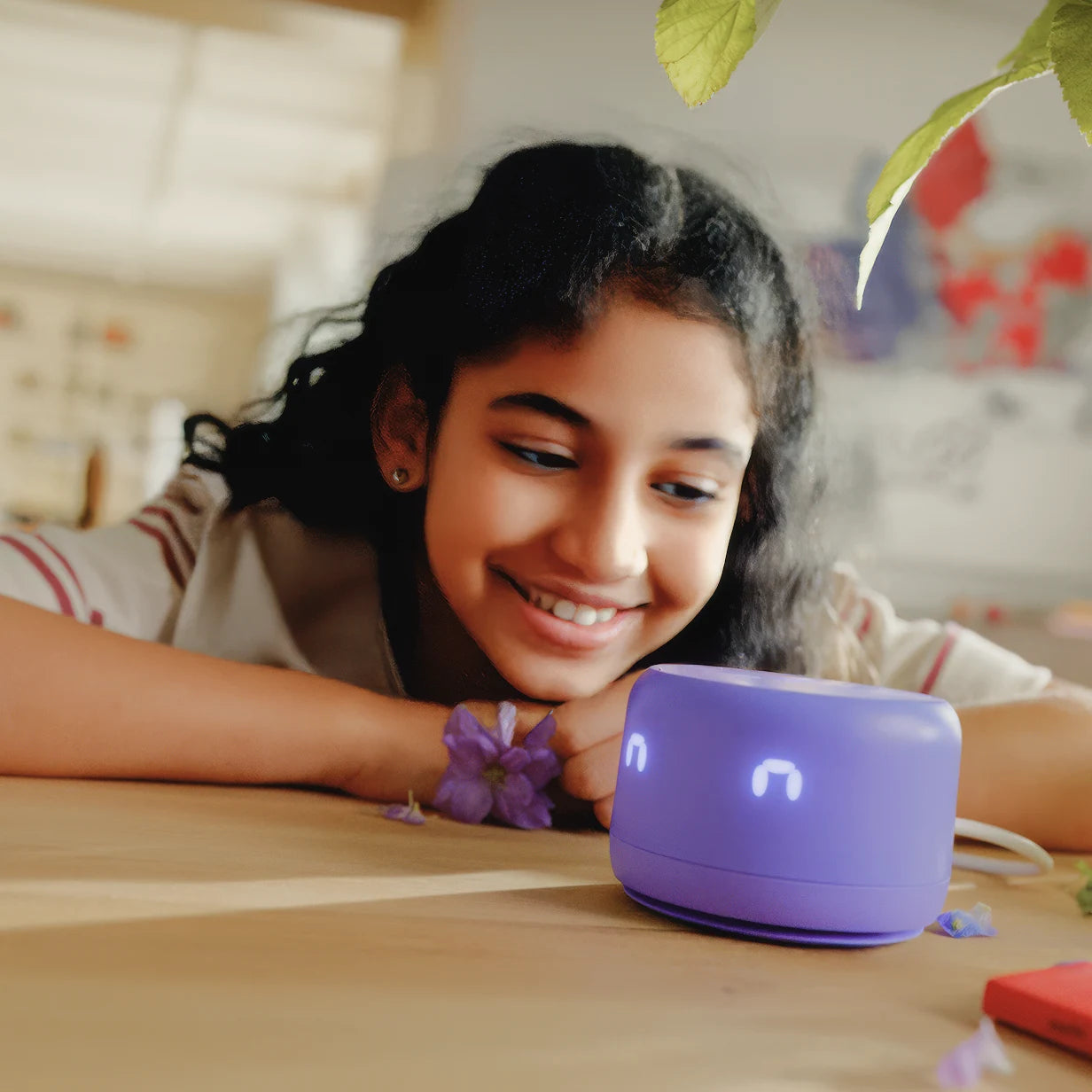 Девочка улыбается, играя с фиолетовой умной колонкой на столе