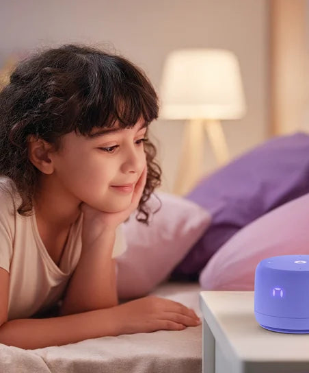 Девочка лежит на кровати и смотрит на умную колонку с экраном