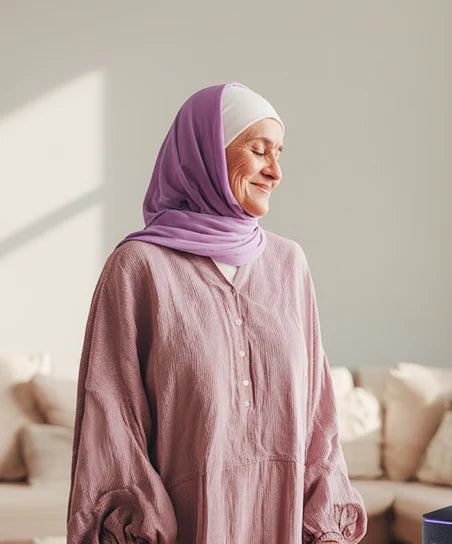 Женщина в хиджабе стоит у окна, мягкое солнечное освещение