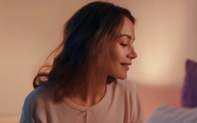 Женщина улыбается, сидя на кровати, тёплый домашний интерьер