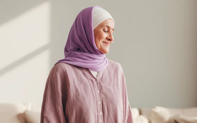 Женщина в хиджабе стоит у окна, мягкое солнечное освещение